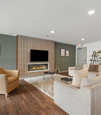 Modern living room with green accent wall, fireplace, TV, beige sofa, armchair, and wooden floor.